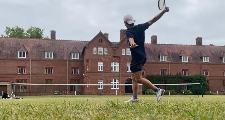 Girton student playing tennis in front of College buildings